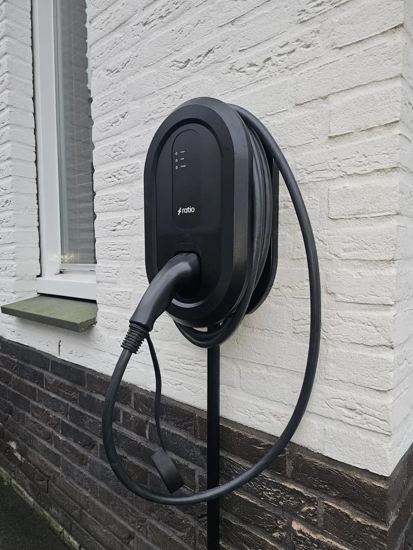 Geïnstalleerd laadstation met opgerolde laadkabel tegen een woning